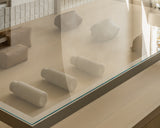 A display case with several kiyo uvc water bottles in castle rock, metro sling, and metro toiletry cases in saddle tan (vegan leather) behind glass. The arrangement is neat, set against a neutral background.
