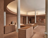 Wide interior of the Monos SoHo store featuring terracotta brick walls, white columns, and tiered seating with aluminum luggage displayed under a softly illuminated curved ceiling.