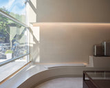 Monos Boston store interior with curved seating by a large front window and silver luggage displayed against a minimalist wall.